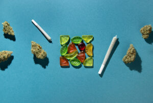 Gummy fruits lie in a square in the center, dry buds of medical marijuana and joints lie to the right and left. Cannabis treatment, On a blue-green background, copy space, flatlay