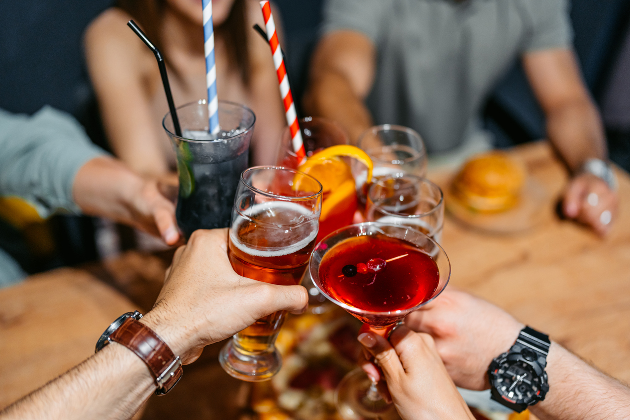 Young group of friends relaxing in a bar,cheering with their alcoholic drinks (cocktails and beer). Close-up.