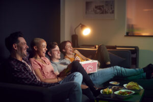 Group Of Friends Eating Popcorn Sitting On Sofa At Home Watching Evening TV And Relaxing Together