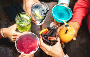 Top view of people hands toasting multicolored fancy drinks - Young friends having fun drinking cocktails at happy hour - Social gathering party concept on vivid filter - Shallow depth of field