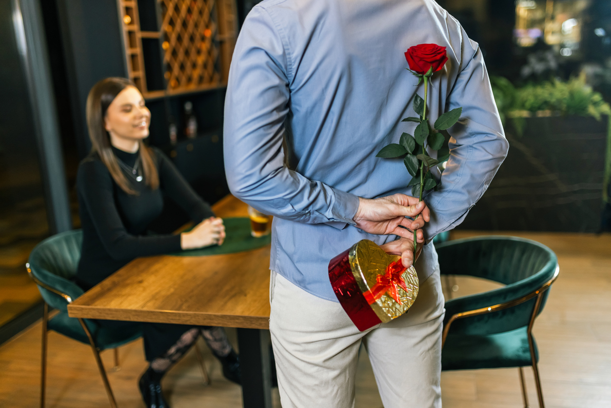 Romantic boyfriend who is about to surprise his girlfriend with red rose and gifts on a romantic dinner date.
