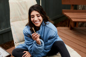 Young woman laughing while sitting alone outside on her patio and smoking a joint