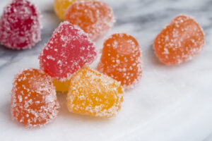 Closeup of gummy candy gumdrops in red, yellow, and orange on a white marble surface. Vitamin supplement or CBD edibles.