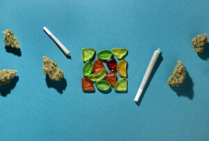 Gummy fruits lie in a square in the center, dry buds of medical marijuana and joints lie to the right and left. Cannabis treatment, On a blue-green background, copy space, flatlay